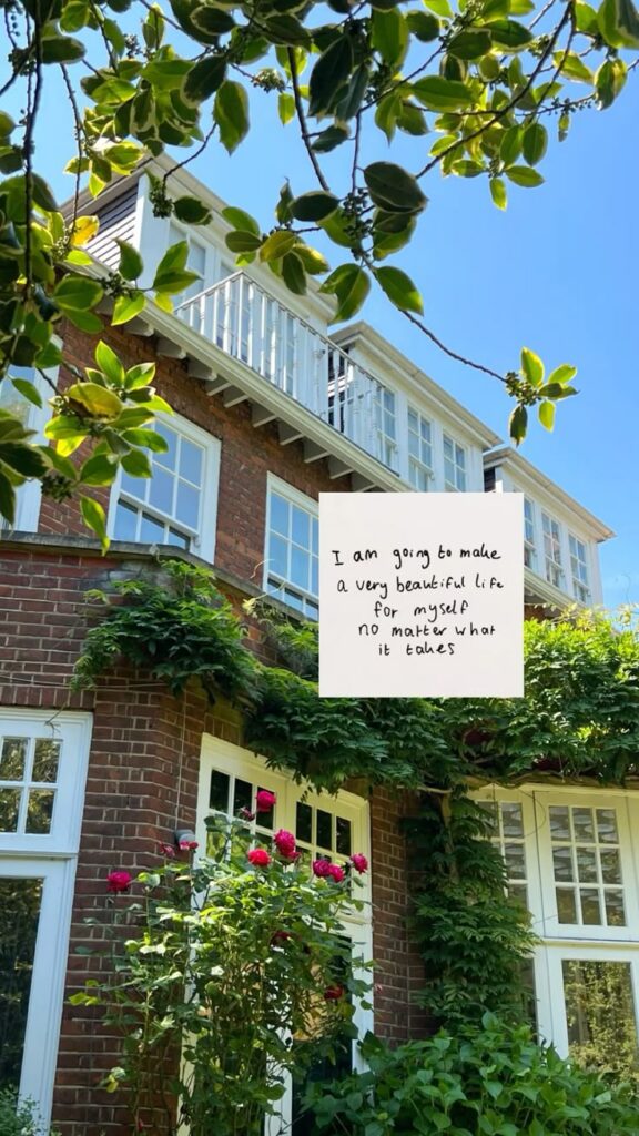 Beautiful brick house with greenery and roses, inspiring handwritten quote overlay: Create a beautiful life.