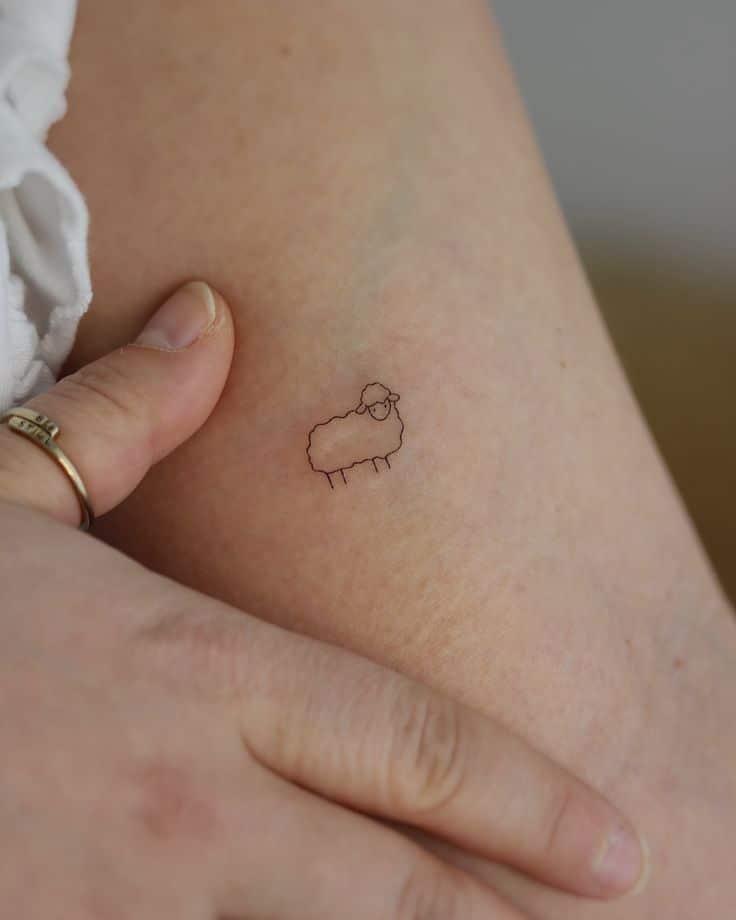 Simple sheep tattoo design on skin with fingers gently touching. Minimalist ink art on arm.