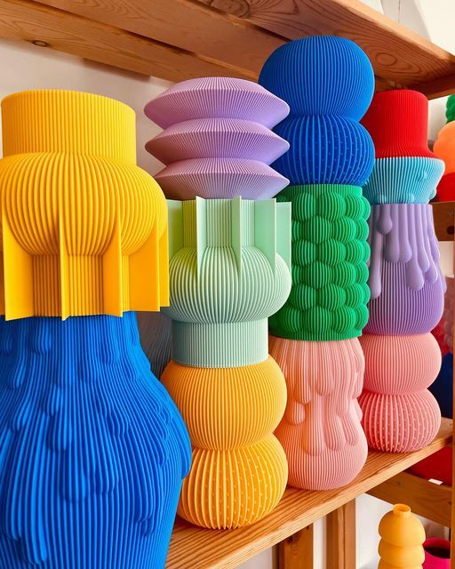 Colorful, ribbed vases on a wooden shelf, showcasing vibrant modern art and design in various shapes and hues.