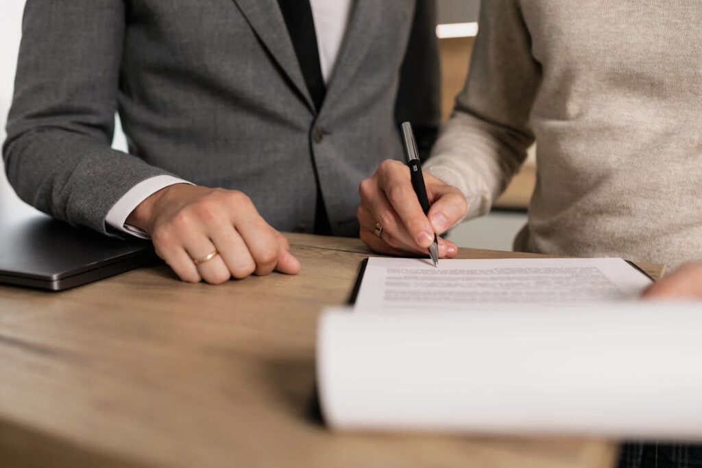 Two people in formal attire signing a document at a wooden desk, symbolizing business agreement.