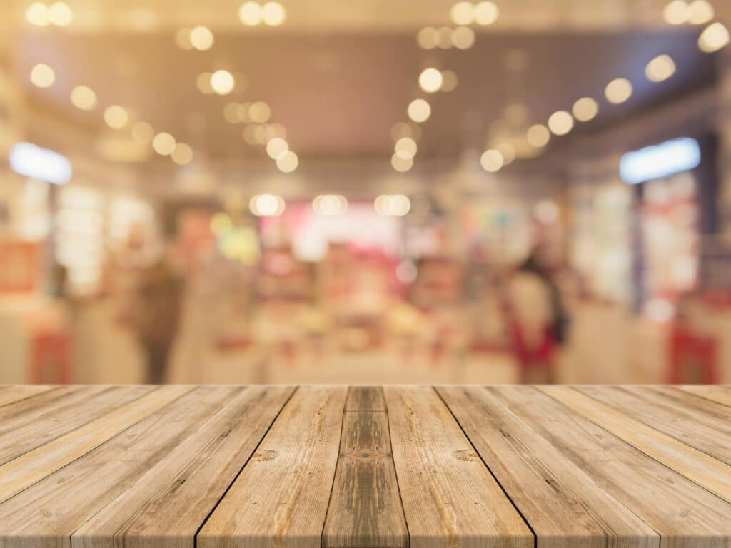 Wooden table with blurred retail store background, showcasing warm lighting and a modern shopping ambiance.