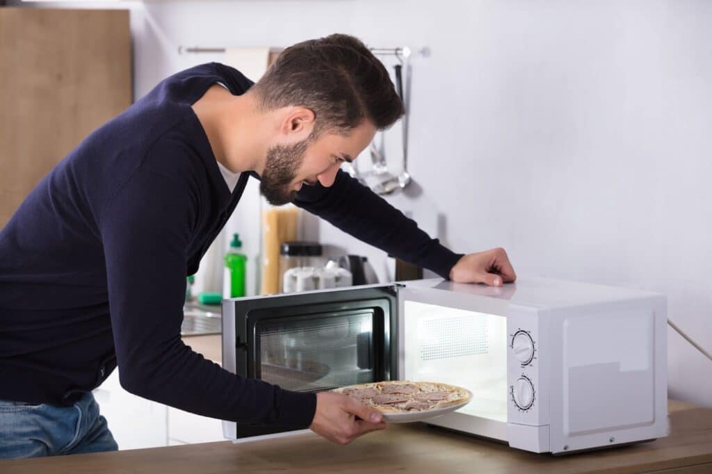 unnamed Man placing a pizza in a microwave in a modern kitchen. | Sky Rye Design Man placing a pizza in a microwave in a modern kitchen.