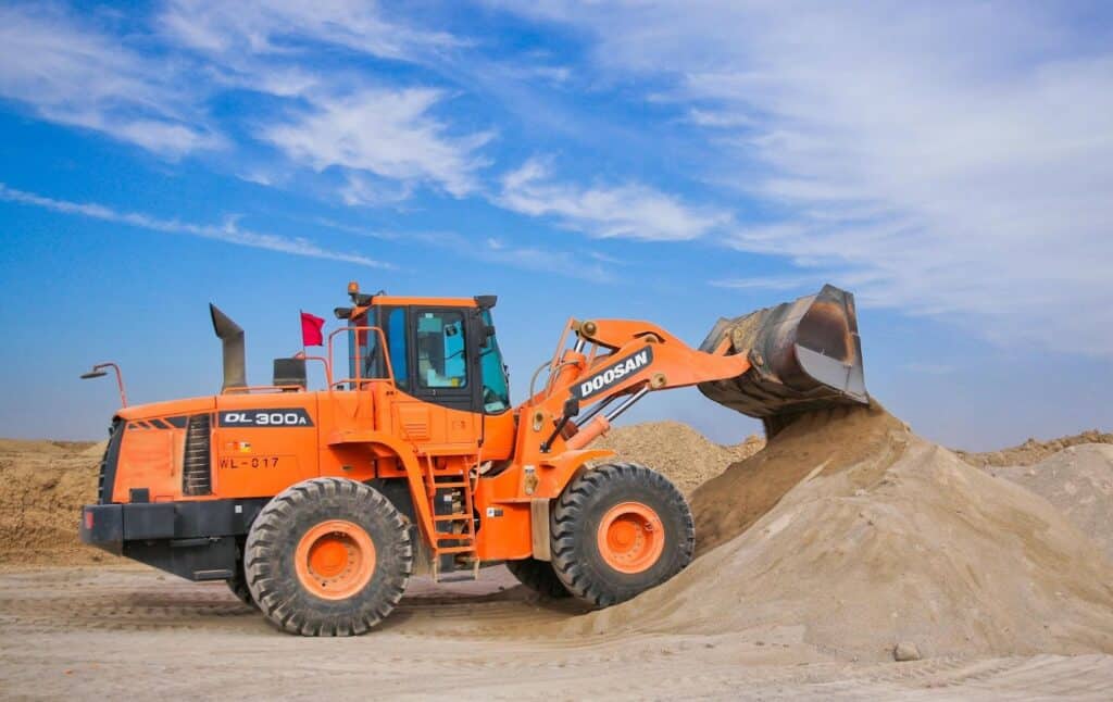 Orange loader moving sand on construction site under blue sky.