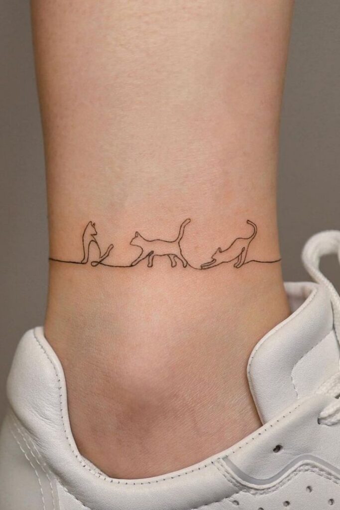 Simple cat line art tattoo wrapped around ankle above white sneaker.