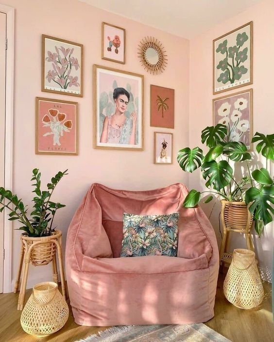 Cozy pink reading nook with lush plants, framed art, and a comfy chair, creating a stylish, serene corner.