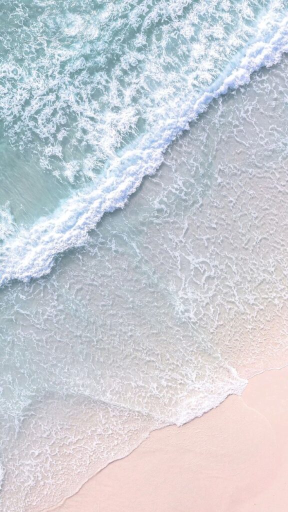 Aerial view of gentle ocean waves washing onto a sandy beach, creating a serene coastal landscape.