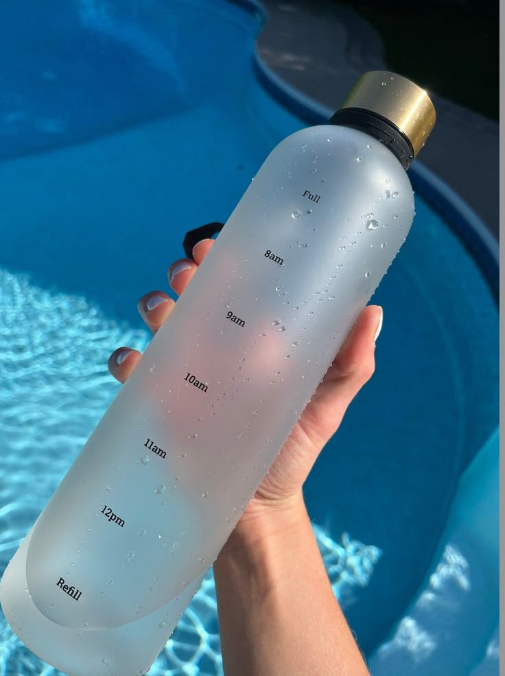 Clear water bottle with time markers held by a hand, poolside background. Perfect for hydration goals and reminders.