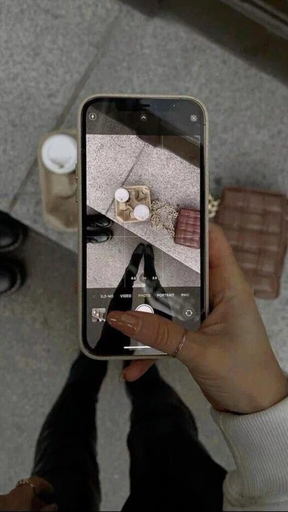 Smartphone captures coffee cups and handbag on pavement, reflected in screen for a creative perspective.