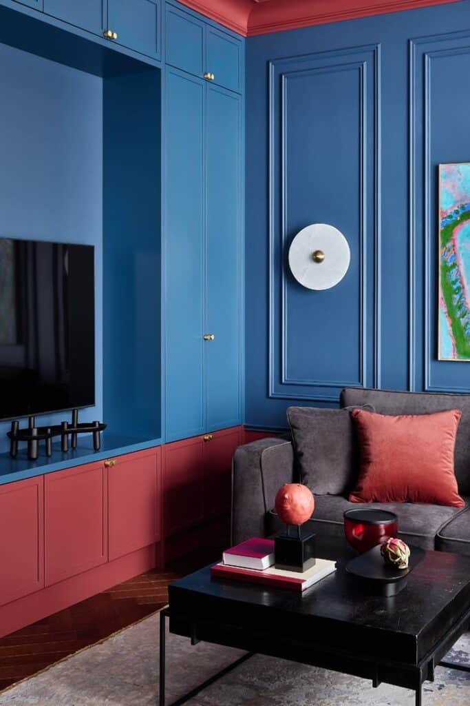 Modern living room with blue and red walls, gray sofa, red pillow, TV, and elegant decor for a stylish interior design.