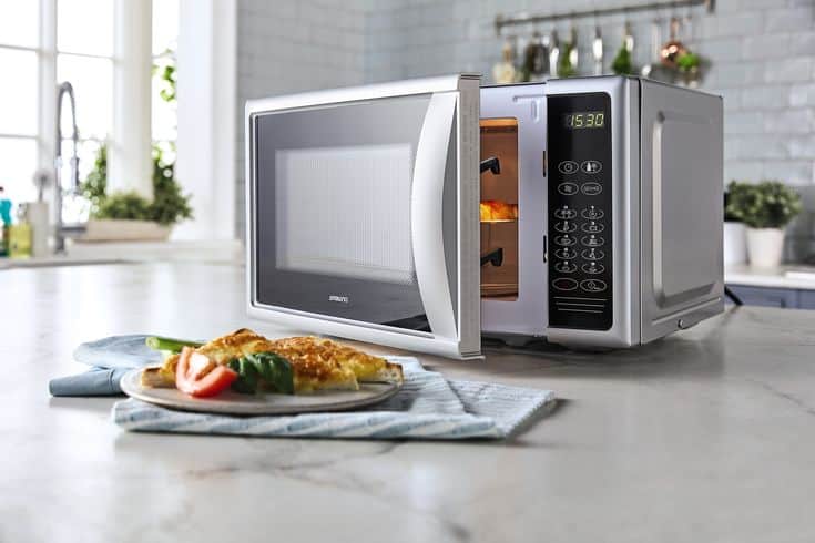 Microwave oven with an open door, displaying cooked food on a kitchen countertop with a plate of food in the foreground.