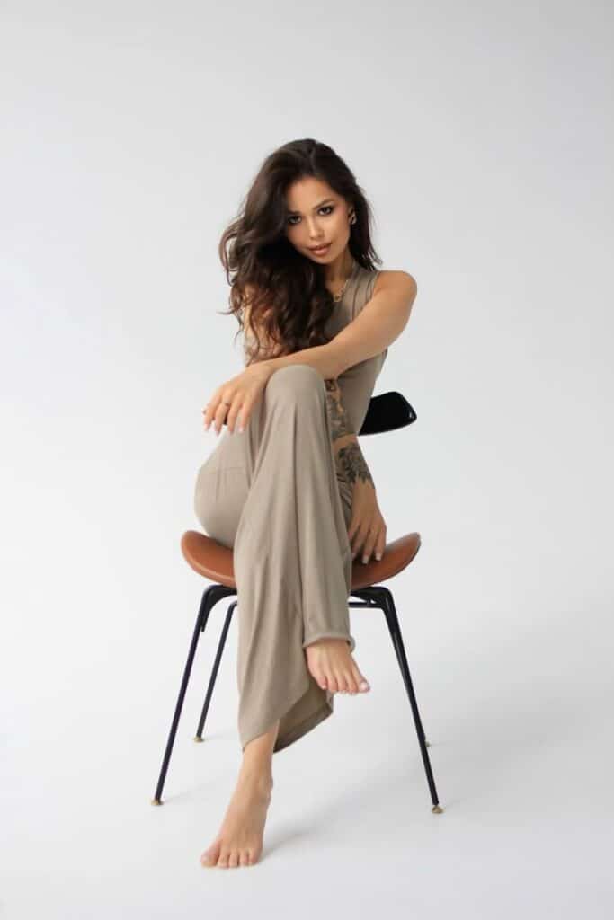 Woman in beige outfit sitting on a chair, posing confidently in a studio setting.