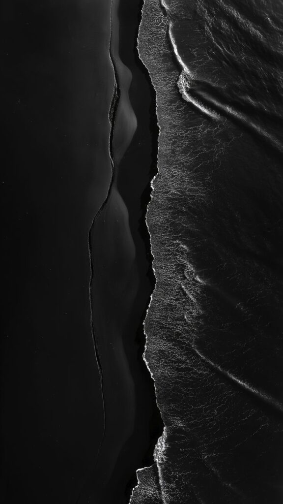 Aerial view of black sand beach and ocean waves in monochrome, showcasing natural contrast and texture.