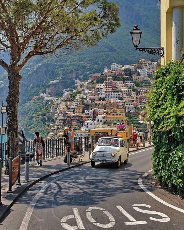 Charming Italian coastal road in Positano with vintage car, vibrant buildings, and scenic sea view.