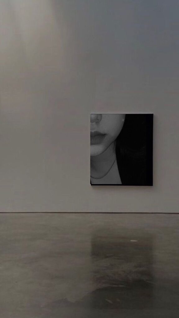 Black and white portrait painting on a minimalist gallery wall with a reflective concrete floor.