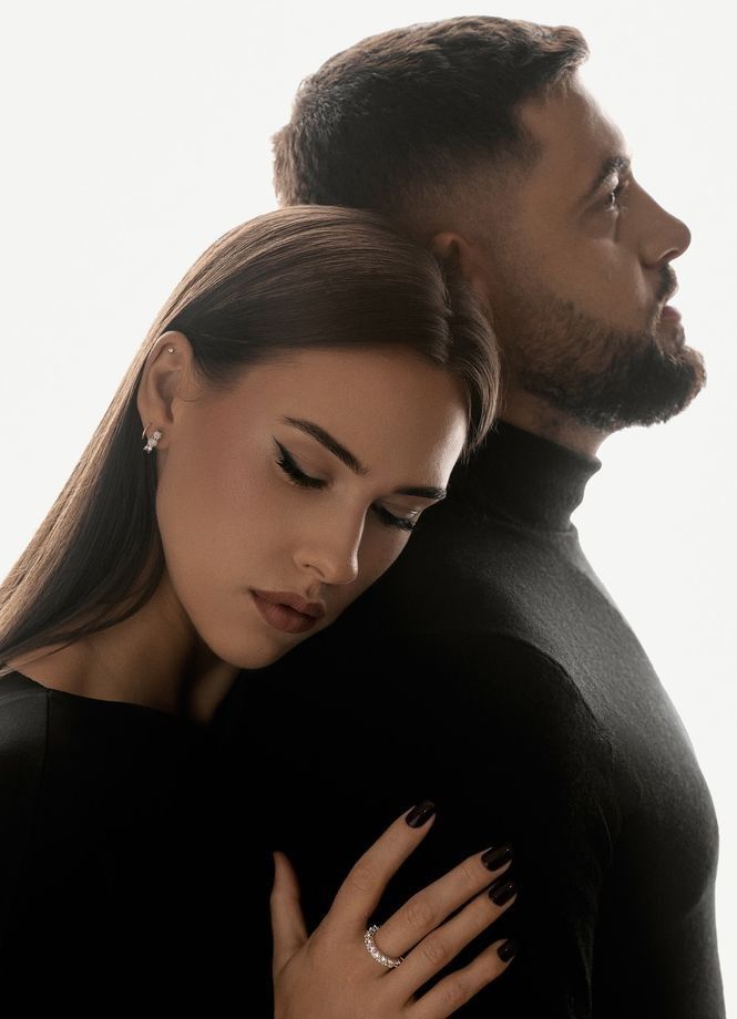 Couple in black clothing, woman rests her head on man's back, showcasing elegance and intimacy.