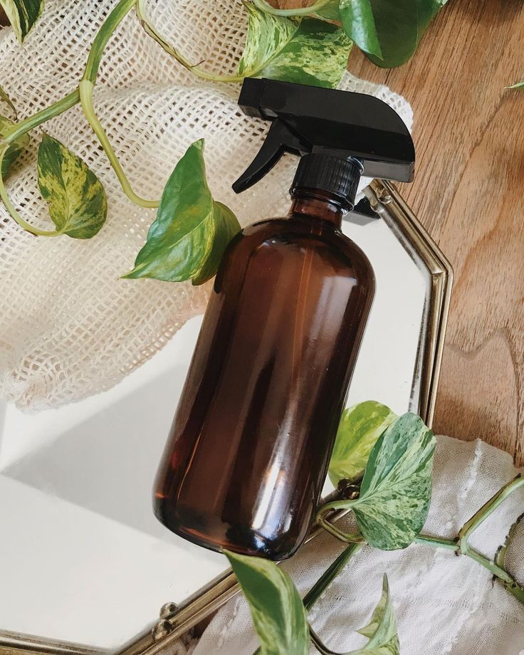 Amber glass spray bottle with plants, placed on a mirrored surface, reflecting natural, eco-friendly home decor.