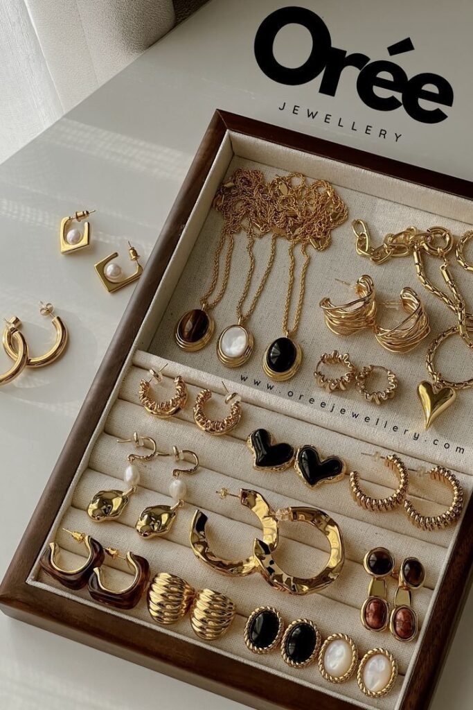 Tray with assorted elegant Orée gold and gemstone jewelry including necklaces and earrings.