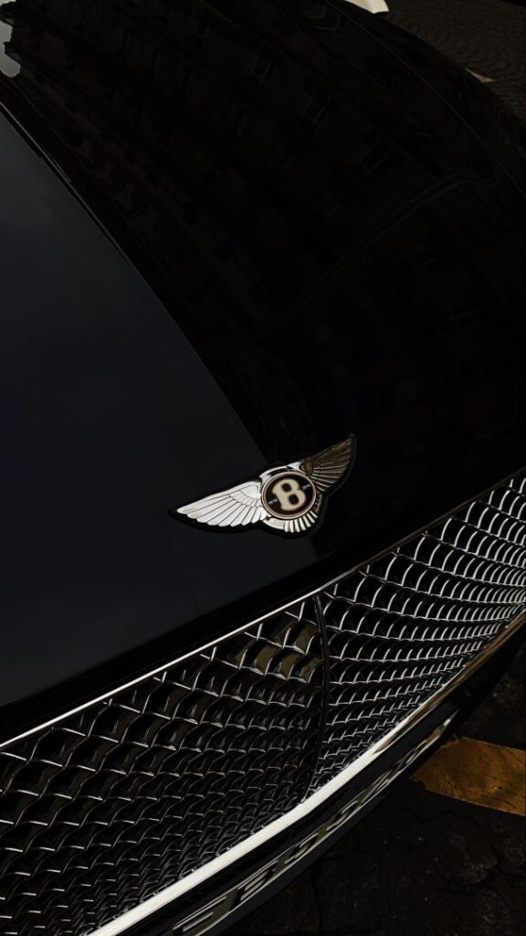 Close-up of a luxury car's front grill and emblem on a shiny black hood.
