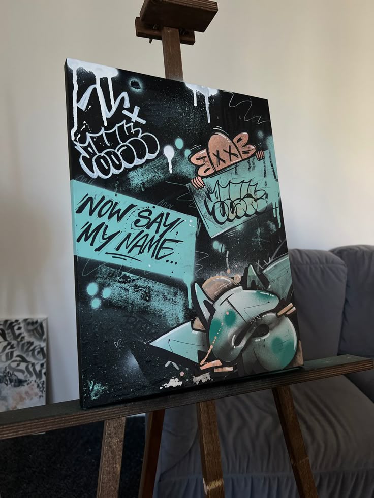 Холст граффити Graffiti-inspired canvas art with abstract design and text Now Say My Name, displayed on an easel. | Sky Rye Design Graffiti-inspired canvas art with abstract design and text Now Say My Name, displayed on an easel.