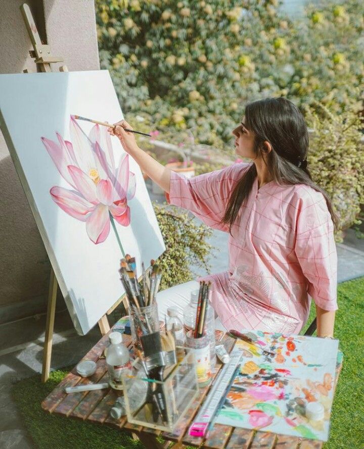 Artist painting a lotus flower in a garden, surrounded by brushes and art supplies on a sunny day.