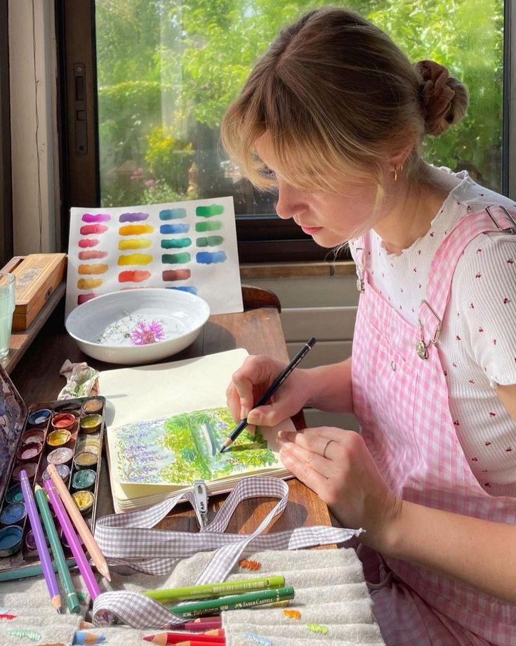 Artist painting with watercolors at a sunlit desk, surrounded by art supplies and vibrant color swatches.