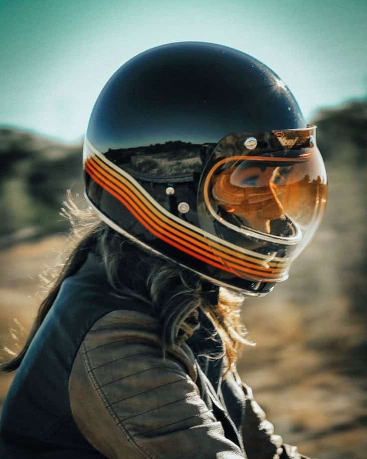 Motorcyclist in retro helmet with orange visor riding on a sunny day.