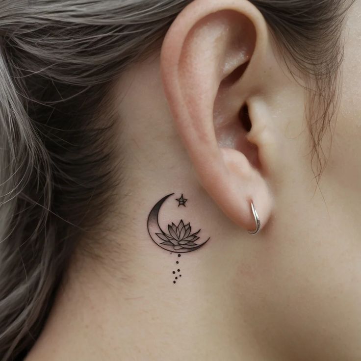 Minimalist crescent moon and lotus tattoo behind ear with star and dots.