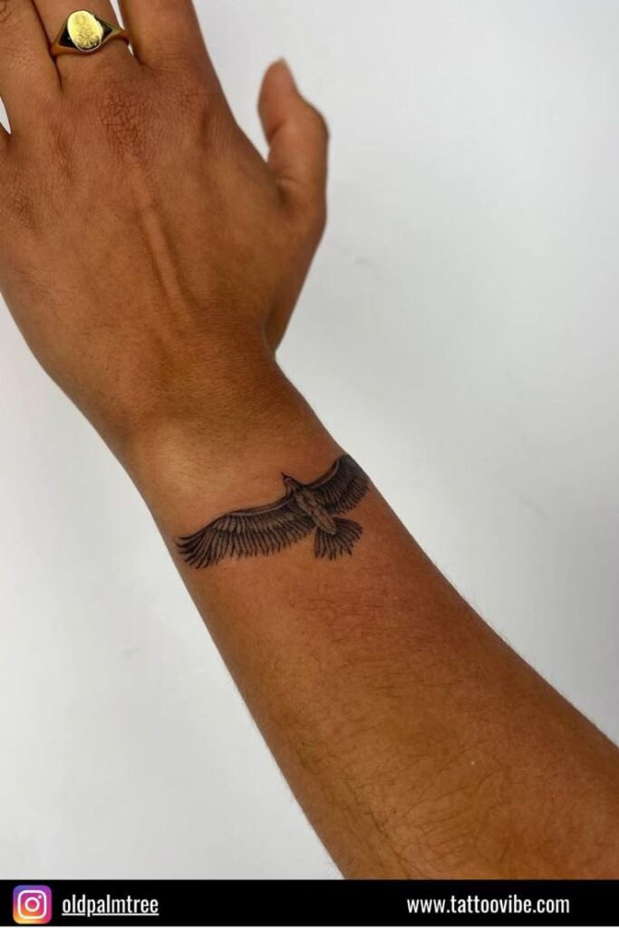 Wrist with a detailed eagle tattoo, showcasing open wings, on a light-skinned arm wearing a gold ring.