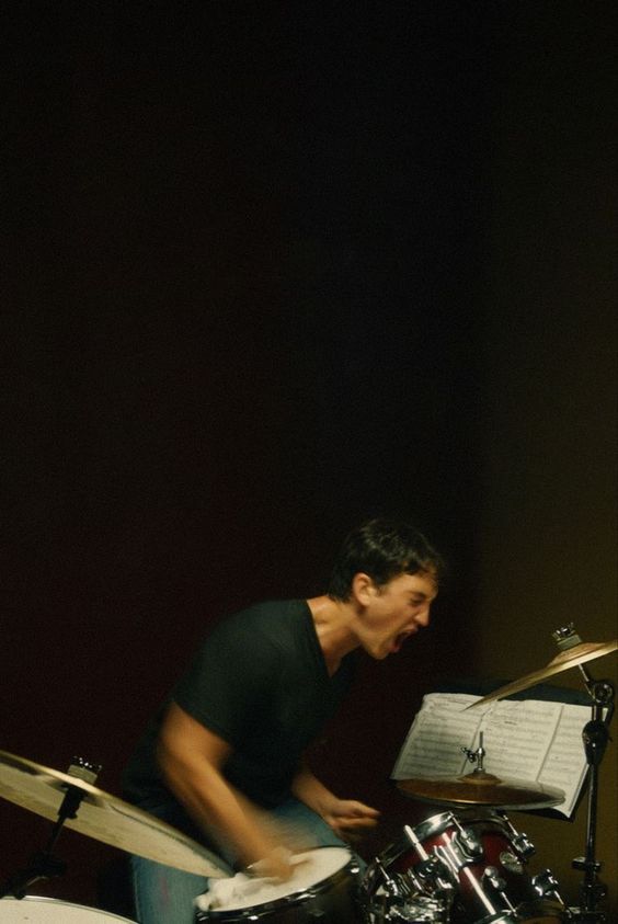 Drummer passionately playing on a drum set with sheet music, expressing intense energy and focus.