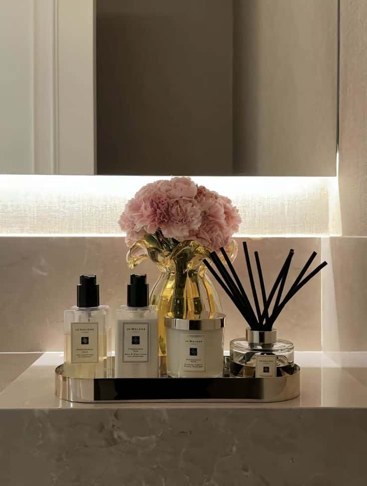 Luxury bathroom décor with pink flowers, elegant fragrance bottles, and scented sticks on a marble countertop.