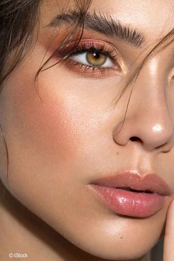 Close-up of a woman's flawless makeup with shimmering eyeshadow, defined brows, and glossy lips.
