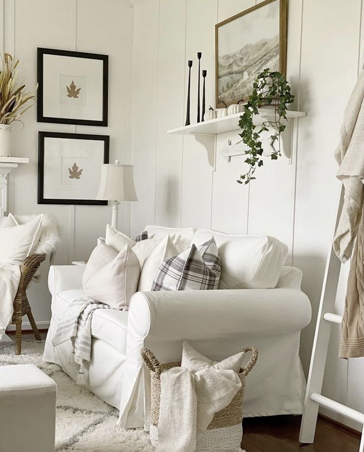 Cozy living room with white sofa, patterned pillows, wall art, and plants, creating a warm, inviting atmosphere.