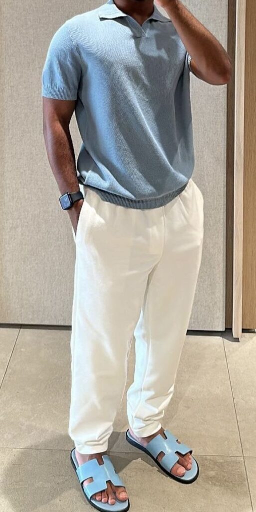 Man in a light blue polo shirt, white pants, and matching blue sandals, accessorized with a smartwatch.