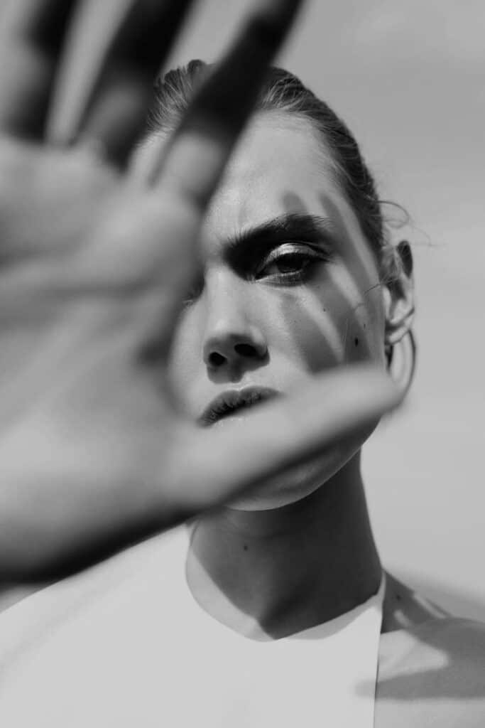 Person shielding face with hand in black and white portrait, conveying emotion and mystery.