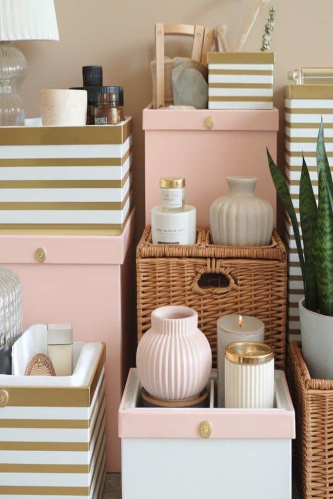 Decorative storage boxes with stripes, candles, pink vases, and green plant create a stylish and organized display.