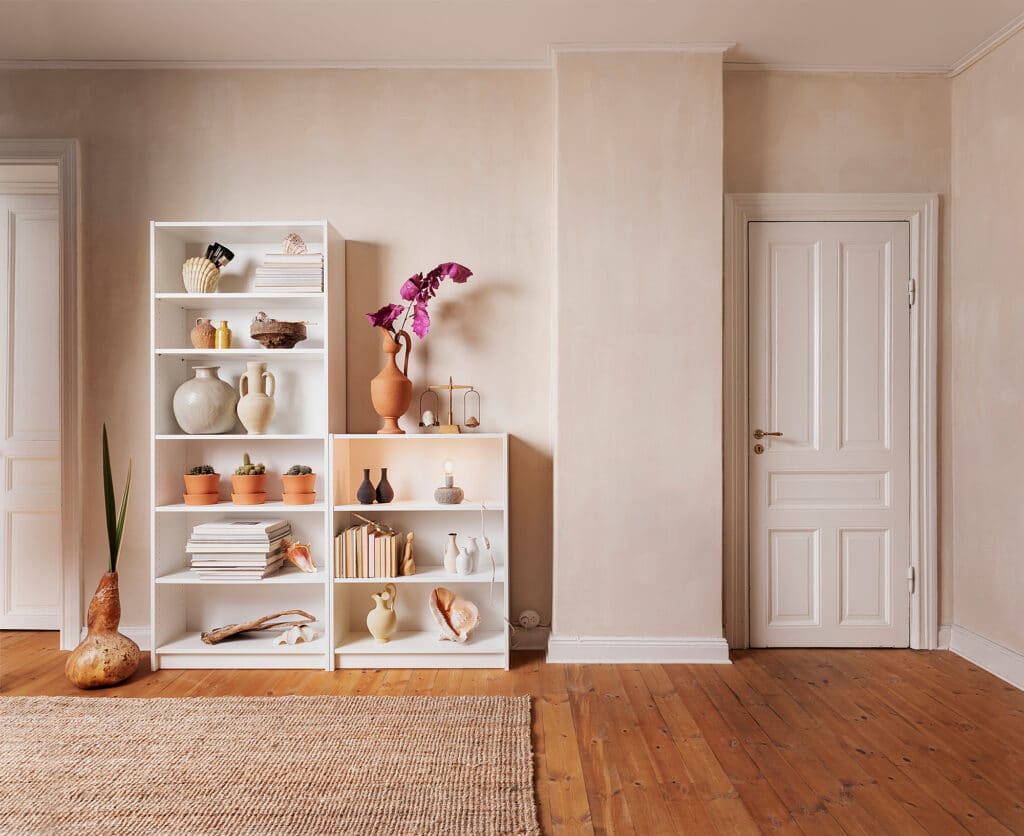 Minimalist room with white bookshelves, terracotta decor, and plants on wooden flooring. Cozy and stylish interior design.