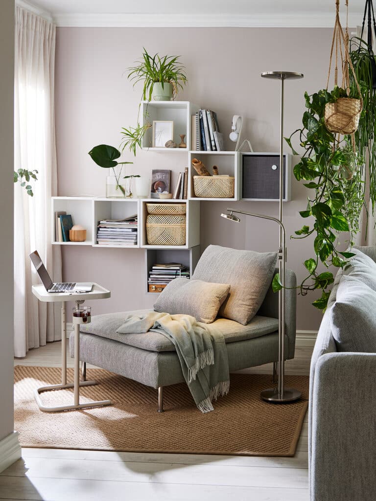 Cozy reading nook with chaise lounge, laptop table, modern shelving, and lush green plants for a serene home office.