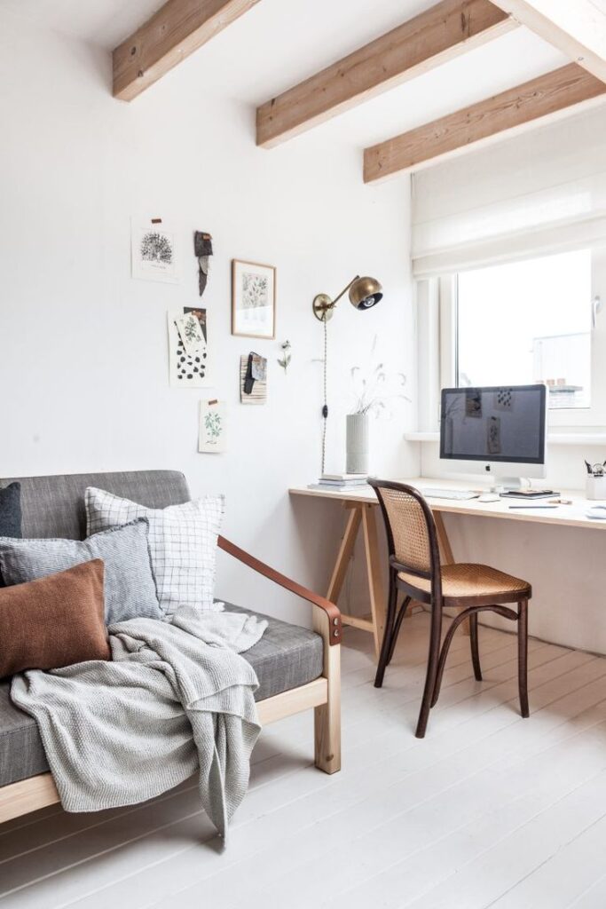 Minimalist home office with a cozy sofa, wooden desk, and wall art, creating a serene work environment with natural light.