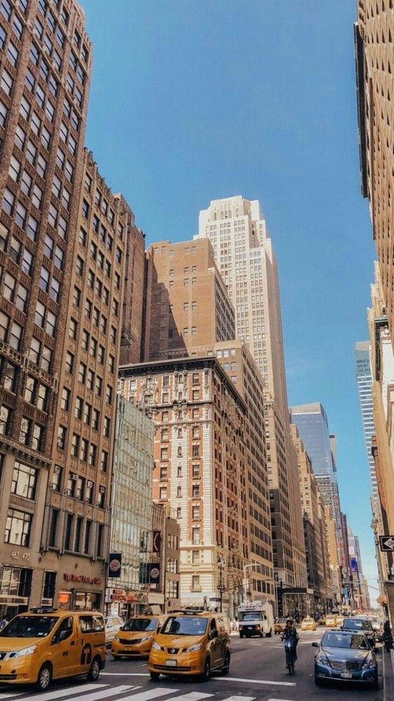 Busy New York City street with yellow taxis and tall buildings under a clear blue sky.