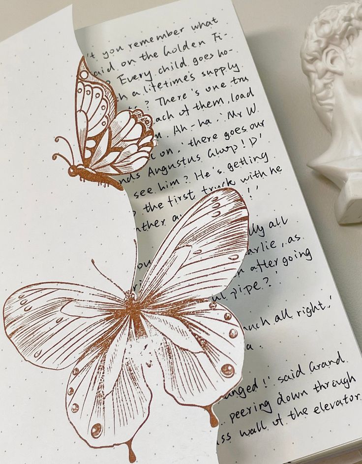 Illustrated butterflies on a notebook with cursive text, next to a white statue. Minimalist aesthetic.