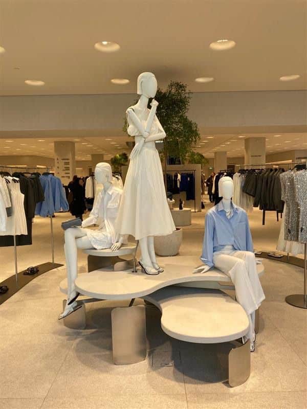 Three mannequins display elegant women's fashion in a modern store setting with stylish outfits and ambient lighting.