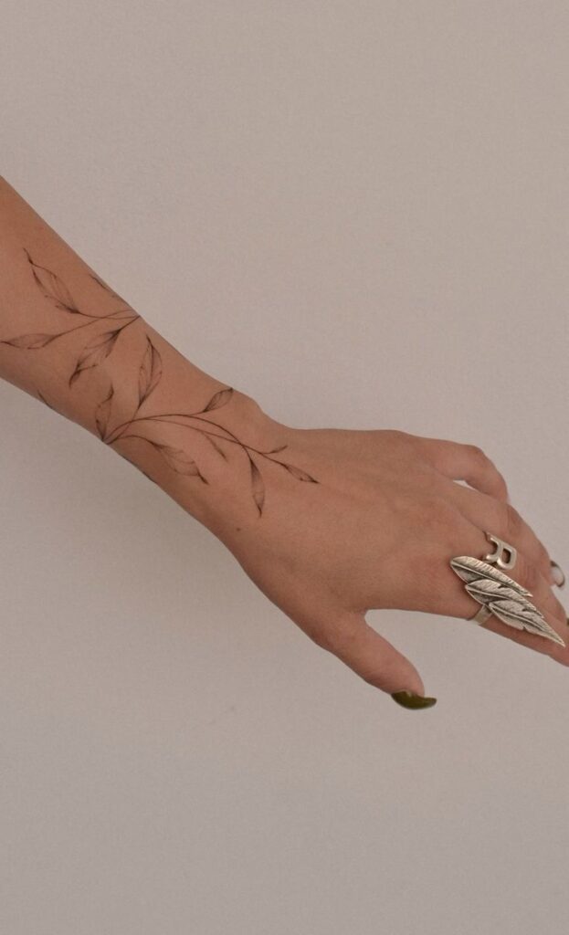 Elegant leaf tattoo on forearm with silver leaf ring, minimalist design, earthy aesthetic.
