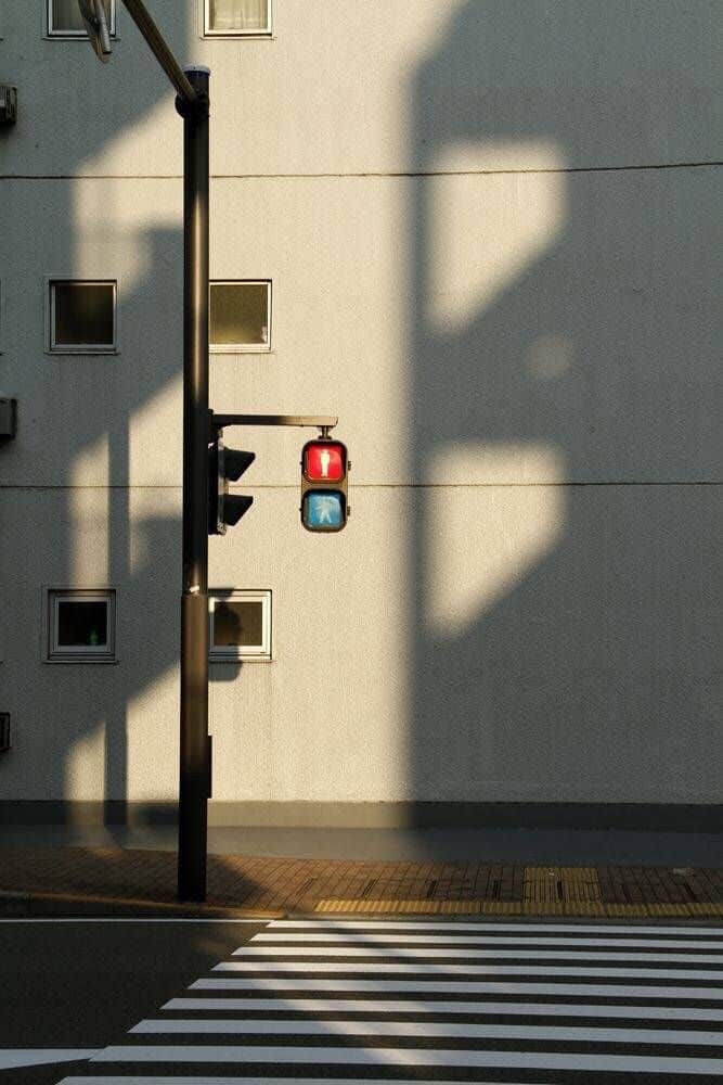 Traffic light above empty crosswalk with building shadows in urban setting.