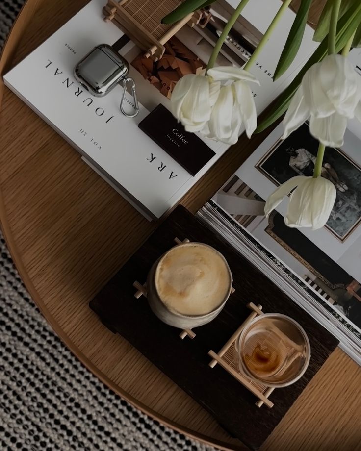Cozy coffee setup on a wooden table with tulips, magazines, and eyeglasses, evoking a peaceful morning ambiance.