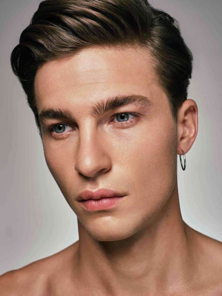 Portrait of a young man with styled hair and hoop earring looking confidently at the camera.