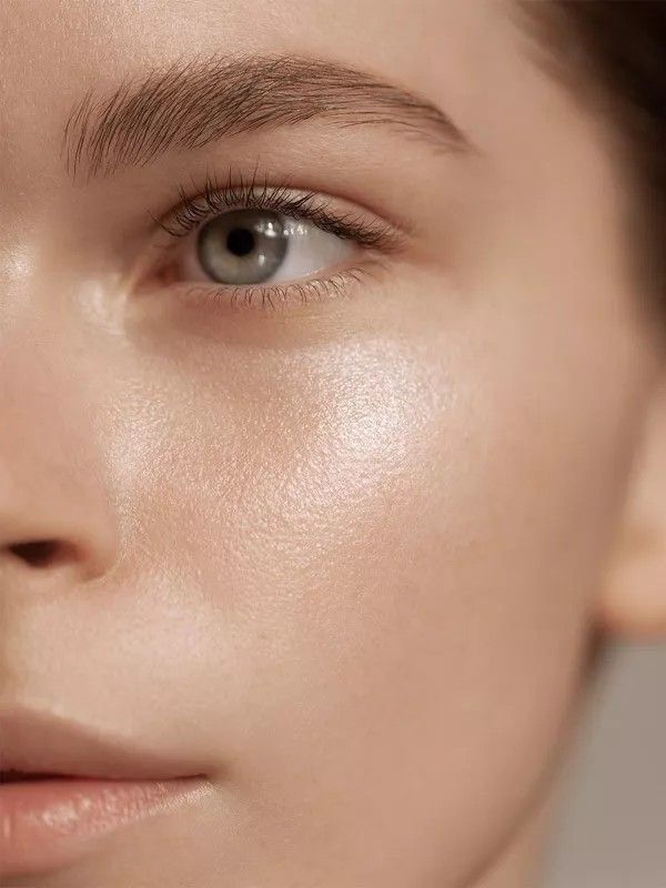 Close-up of a person's face with smooth, glowing skin, highlighting a well-groomed eyebrow and clear complexion.