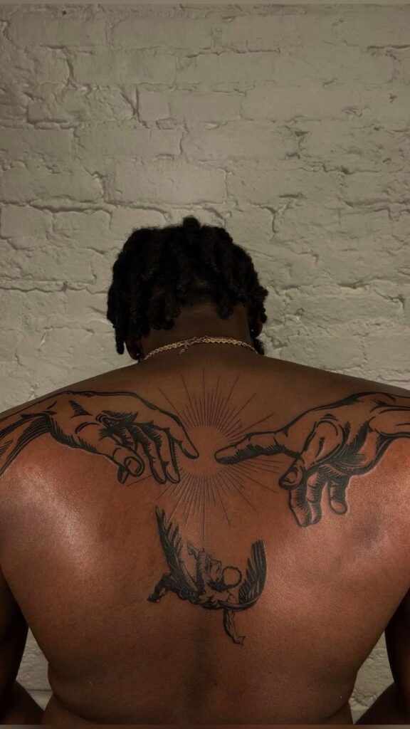 Back tattoo with hands reaching out and an angel on a textured wall backdrop.
