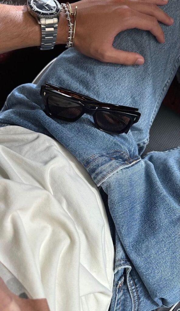 Casual style: person in jeans and white tee, silver watch, with sunglasses on lap.
