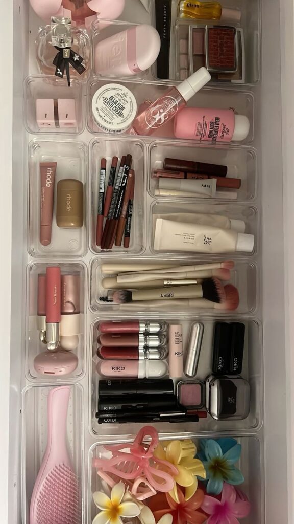 Organized makeup drawer with lipsticks, brushes, and floral hair clips in clear compartments.
