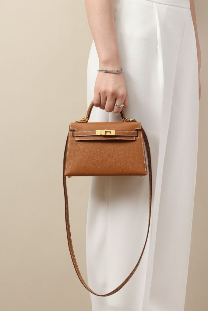 Elegant brown leather handbag held by a woman in white pants, showcasing style and sophistication.